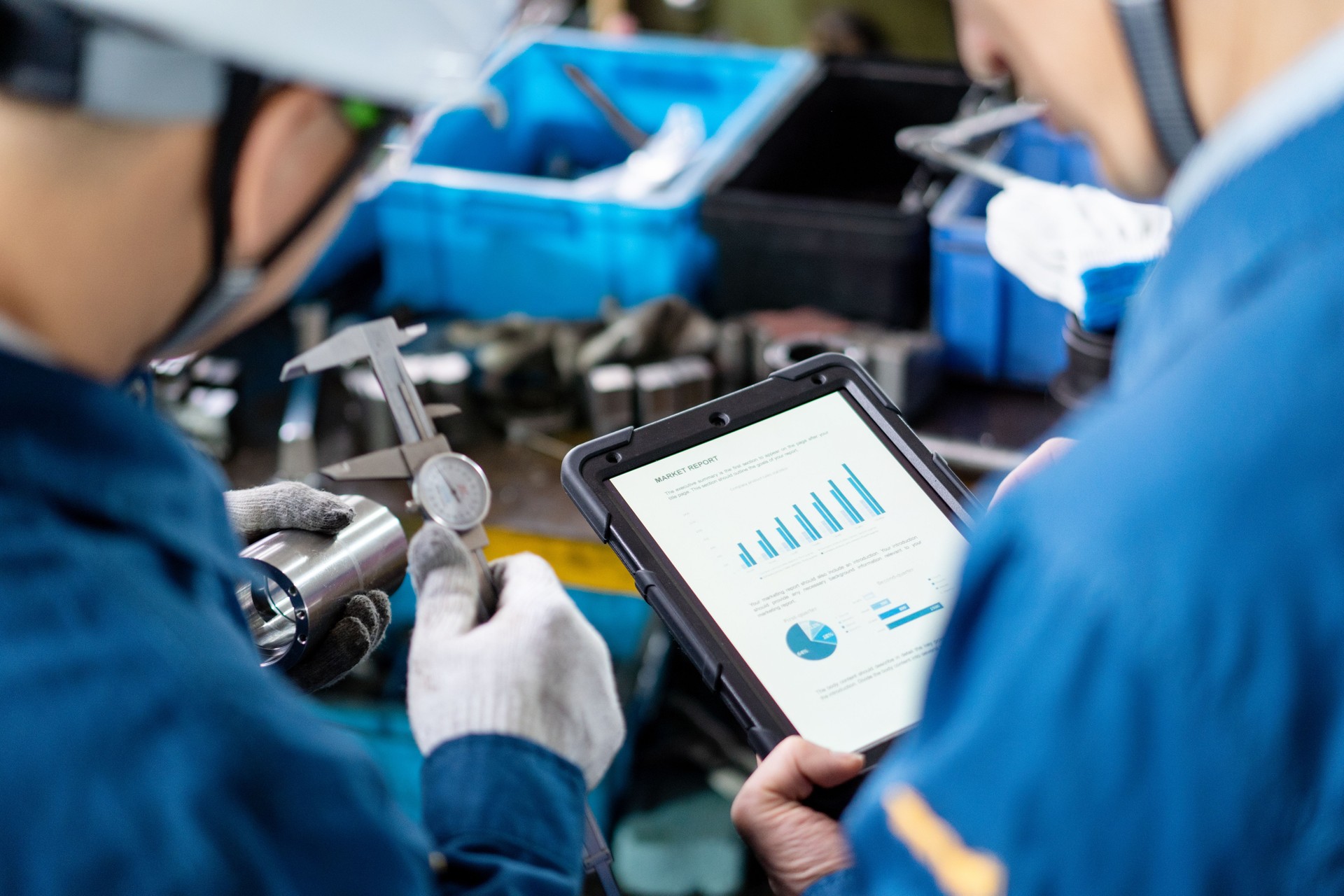 An Asian male worker is working in the factory workshop while holding a tablet computer with data analysis reports.